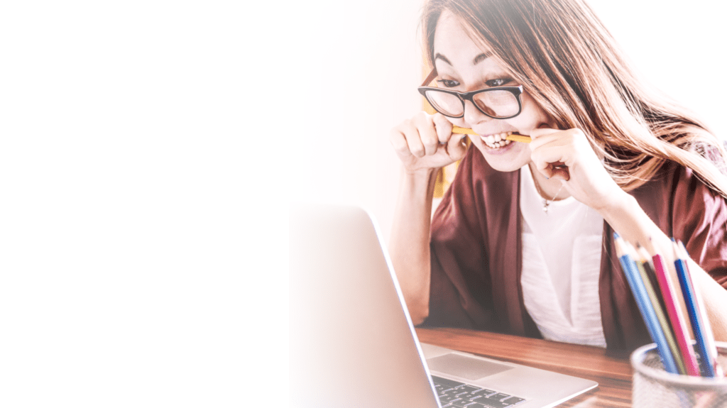 Photo of a frustrated woman biting her pencil while looking at her computer screen.
